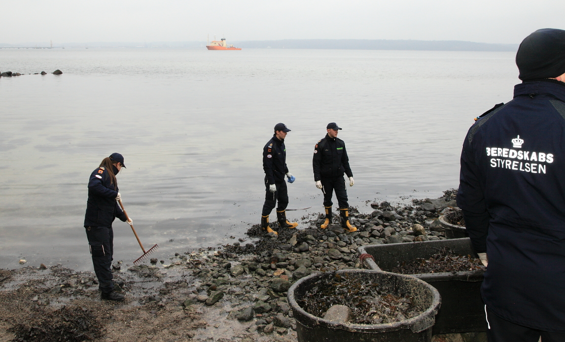 På billedet ses værnepligtige på assistance til en olieforurening ved Aabenraa. I baggrunden ses miljøskibet Gunnar Seidenfarden på opgave på det dybe vand.